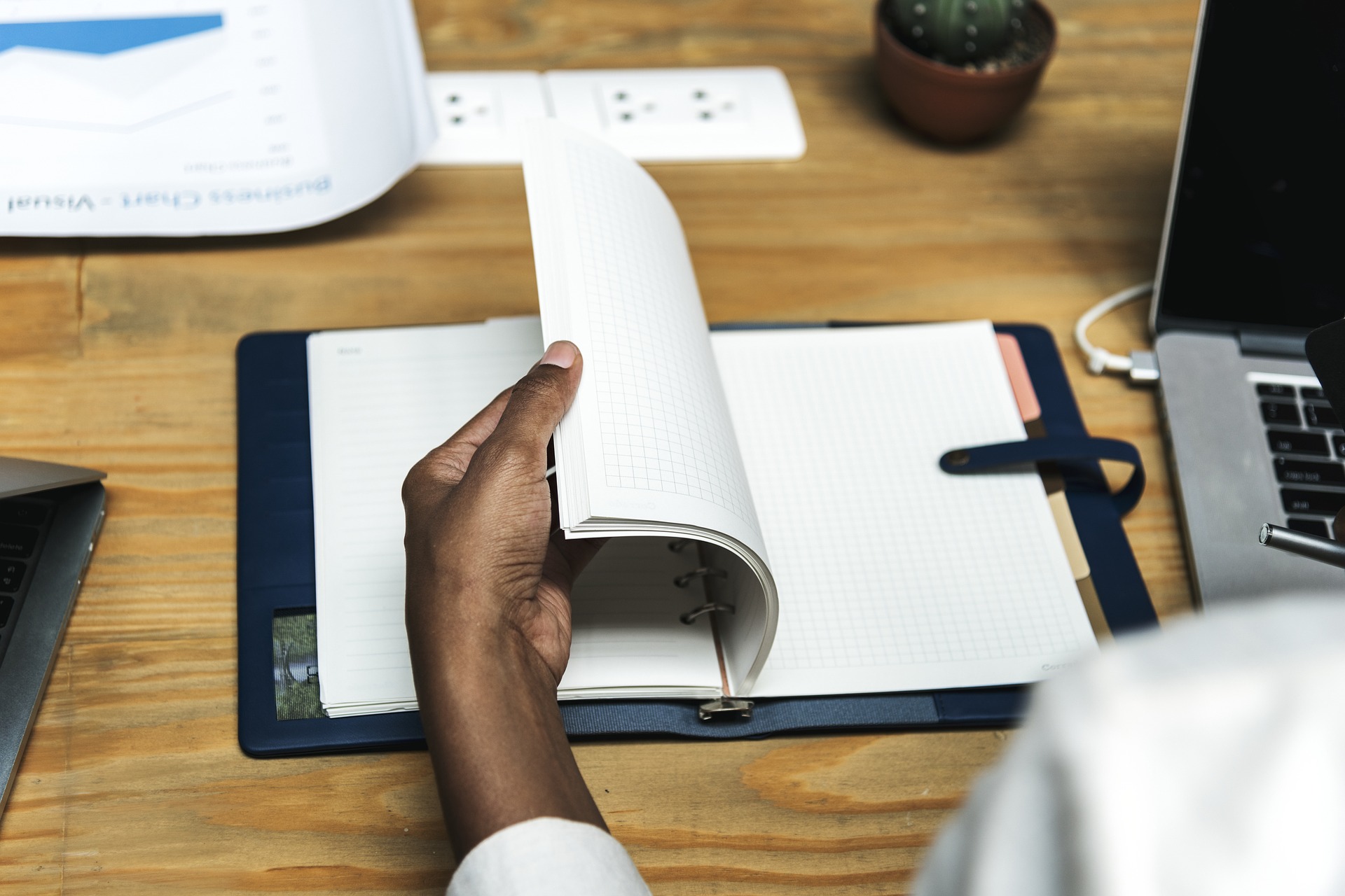 Man's left hand flipping through social media content planner on wood table