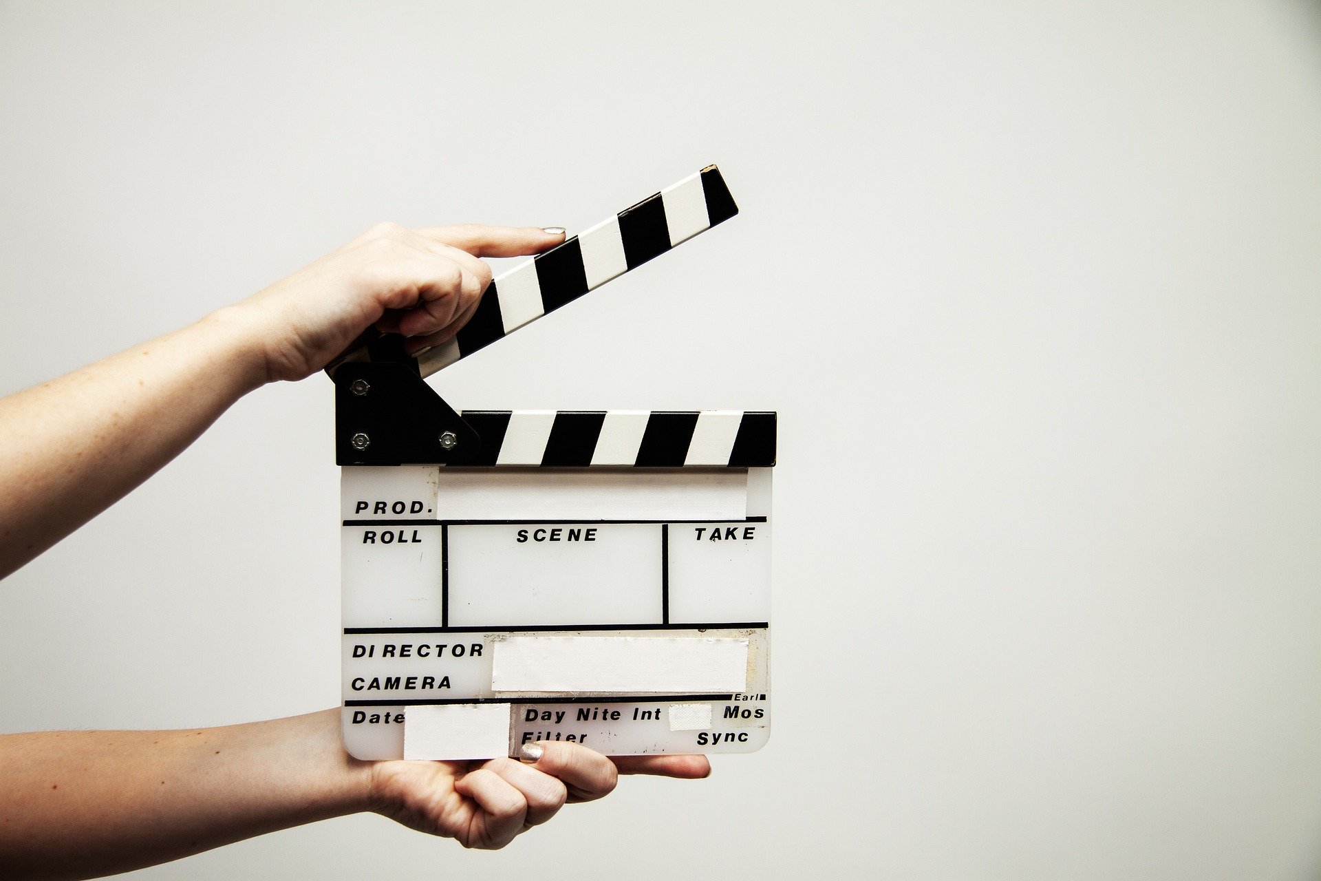 Two hands holding a video clapperboard against a white wall